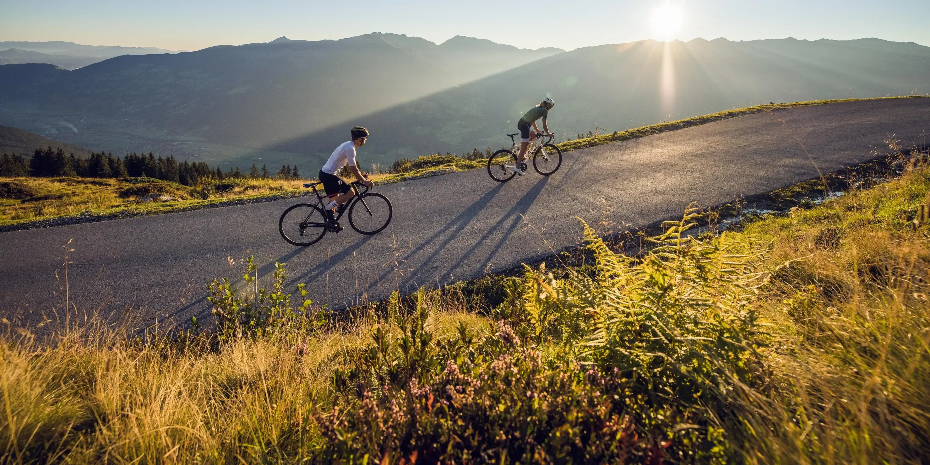 Cyclistes sur une route de col au lever du soleil